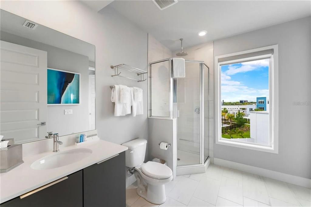 A modern bathroom features a vanity, toilet, glass-enclosed shower, and a window with exterior views — 7740 SANDY RIDGE DRIVE UNIT 211, REUNION, FL