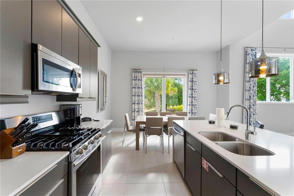 A modern kitchen with dark cabinets, white countertops, and a dining area overlooking palm trees — 7740 SANDY RIDGE DRIVE UNIT 211, REUNION, FL