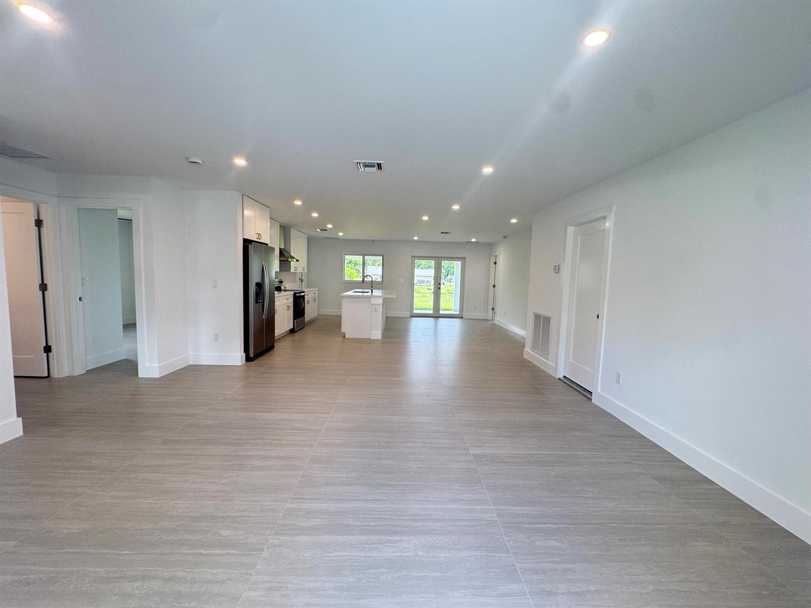 An open-concept kitchen and living area features white cabinetry, stainless appliances, and gray tile flooring — 13177 47th Court N, FL 33411, FL