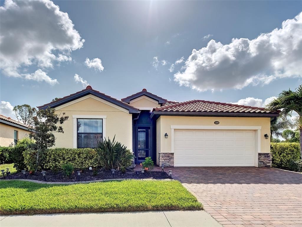 A single-story house with a beige stucco exterior, tile roof, and a two-car garage — 12390 CINQUETERRE DRIVE, VENICE, FL