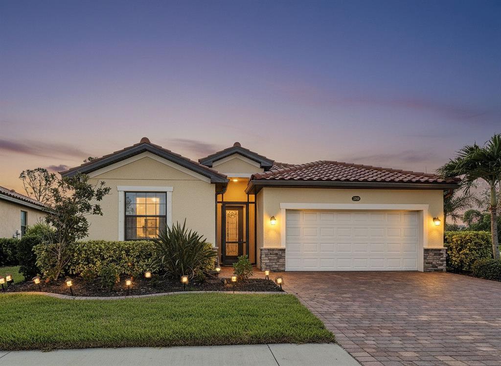 A single-story house with a tiled roof, stucco exterior, and a paved driveway at dusk — 12390 CINQUETERRE DRIVE, VENICE, FL