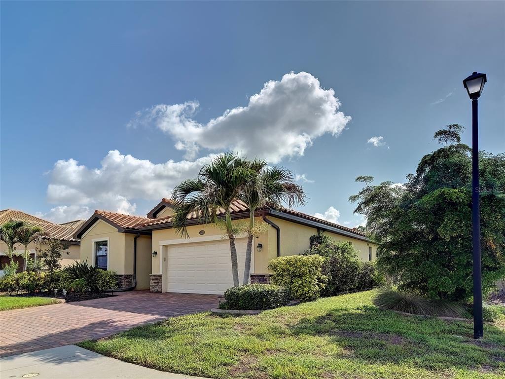 A single-story house with a tan stucco exterior, tile roof, and a two-car garage — 12390 CINQUETERRE DRIVE, VENICE, FL