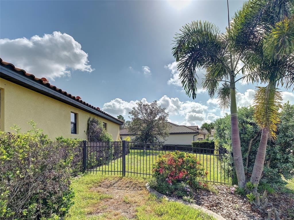 A fenced backyard features a palm tree, landscaping, and a view of neighboring houses — 12390 CINQUETERRE DRIVE, VENICE, FL