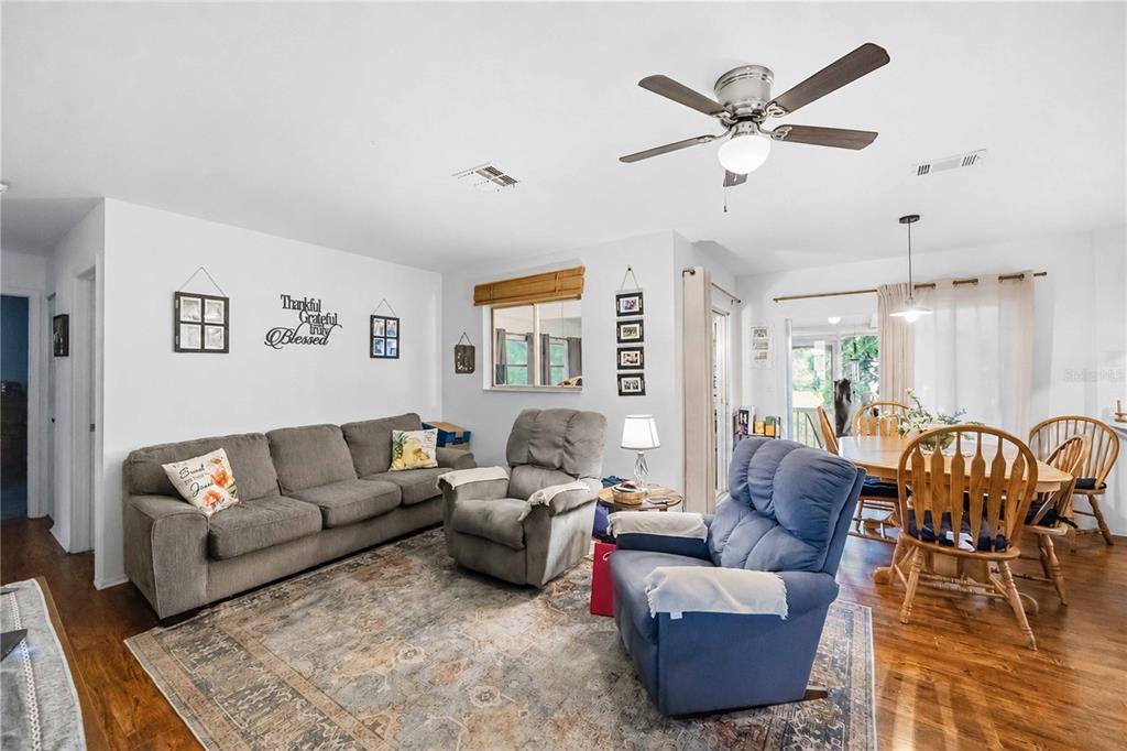 A living room with a gray sofa, two recliners, a dining area, and hardwood floors — 5409 KENWOOD DRIVE, NORTH PORT, FL