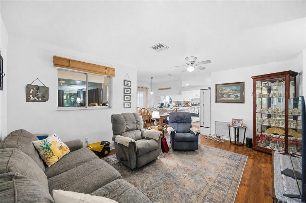 A living room with a gray sofa, two recliners, a display cabinet, and wood flooring — 5409 KENWOOD DRIVE, NORTH PORT, FL