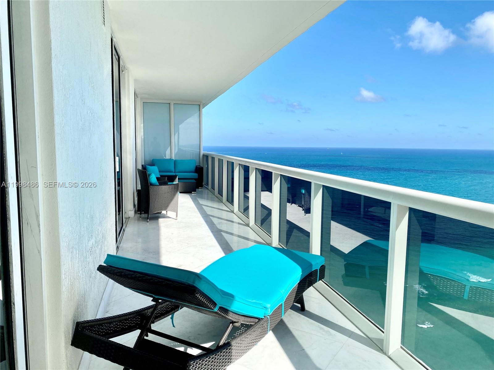 A balcony with a lounge chair and seating overlooks the ocean with a glass railing — 1830 S Ocean Dr # 3203, Hallandale Beach FL 33009, HALLANDALE BEACH, FL