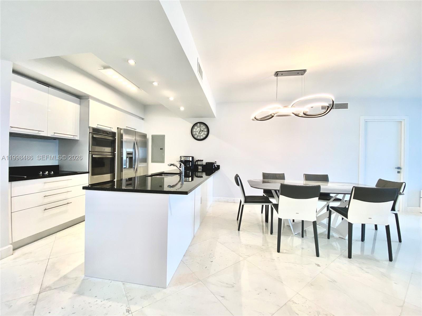 A modern kitchen and dining area features white cabinetry, black countertops, and marble flooring — 1830 S Ocean Dr # 3203, Hallandale Beach FL 33009, HALLANDALE BEACH, FL