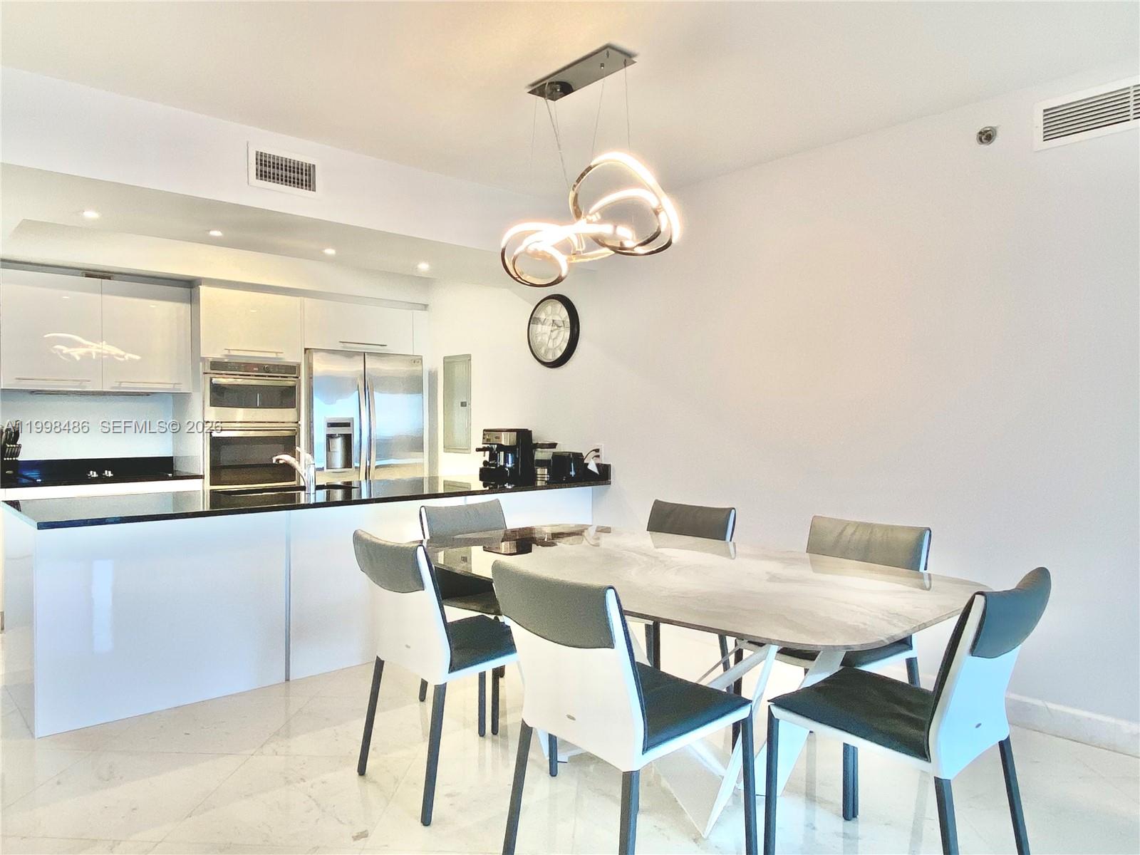 A dining area with a marble-topped table and modern chairs sits beside a white kitchen — 1830 S Ocean Dr # 3203, Hallandale Beach FL 33009, HALLANDALE BEACH, FL