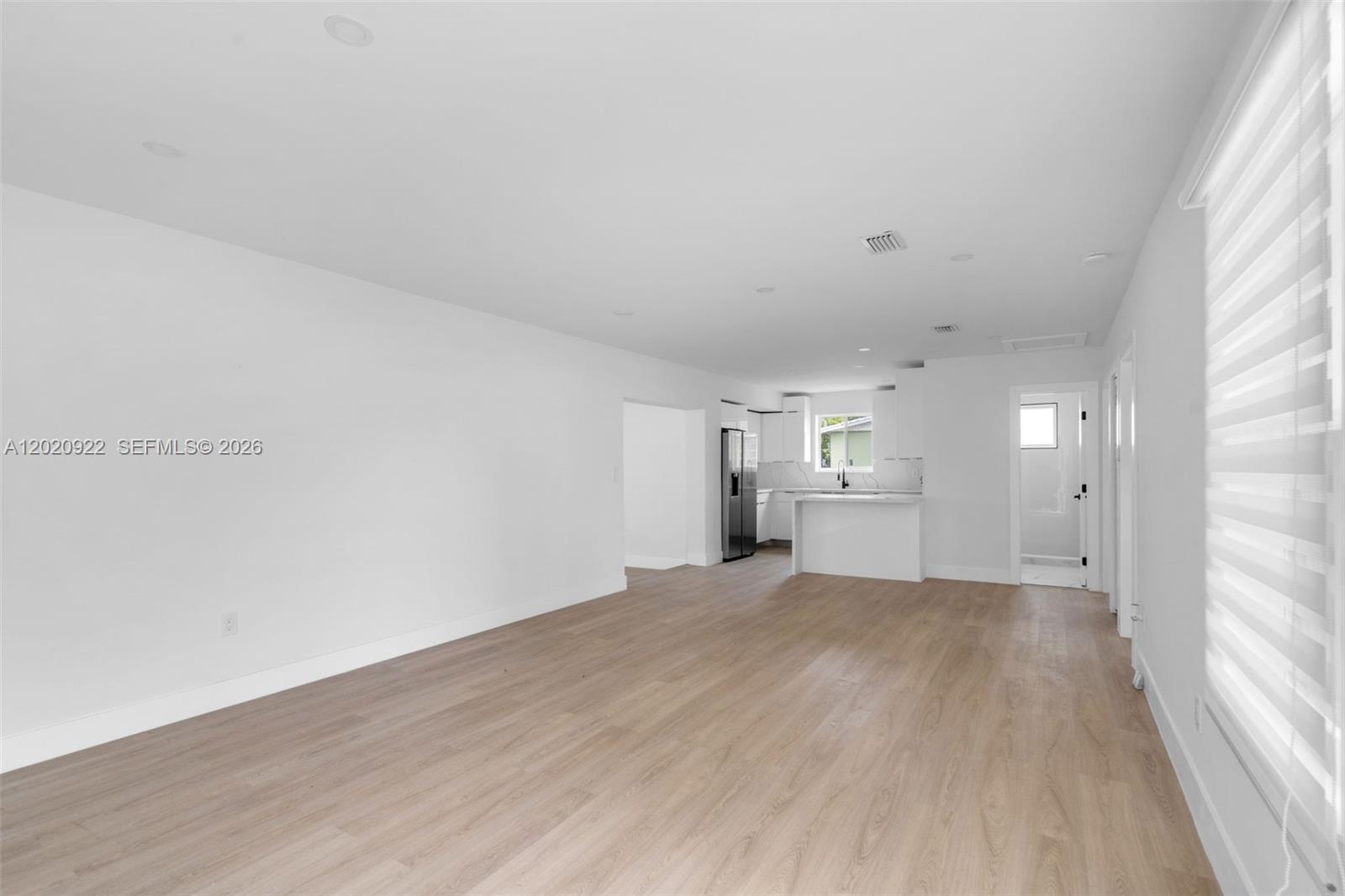 An open-concept living area features light wood-look flooring, white walls, and a modern kitchen — 17231 NW 24th Pl, Miami Gardens FL 33056, MIAMI GARDENS, FL