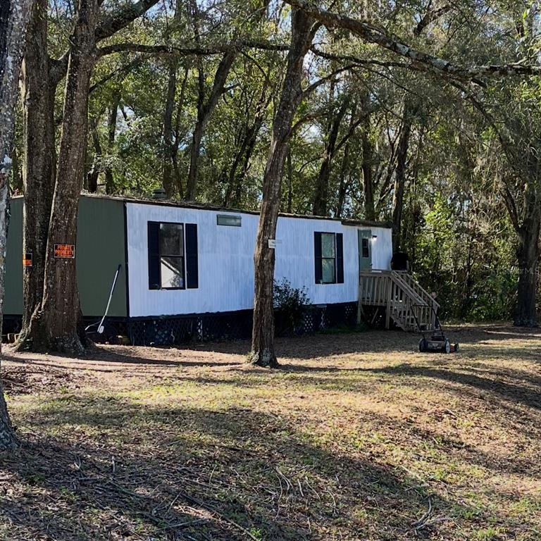A single-story mobile home with white siding and black shutters sits in a wooded lot — 6359 VASSAR DRIVE, KEYSTONE HEIGHTS, FL