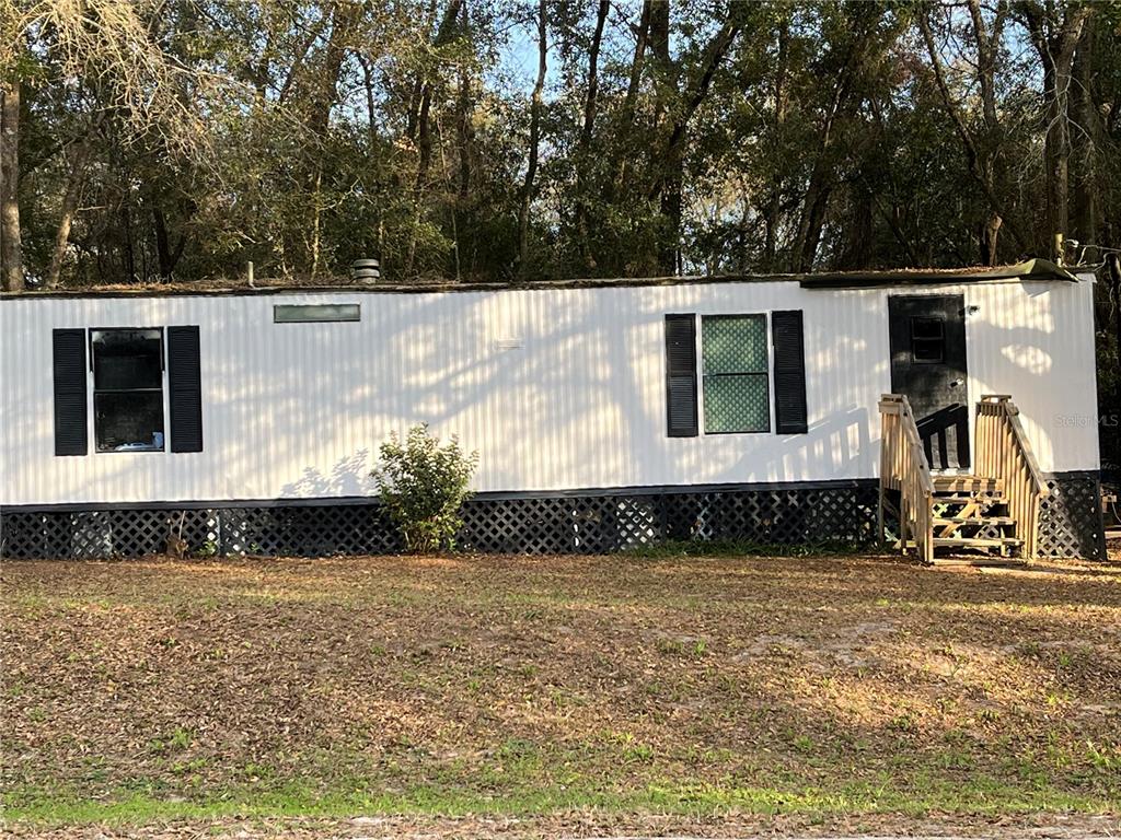 A single-story mobile home with white siding, black shutters, and wooden stairs sits outdoors — 6359 VASSAR DRIVE, KEYSTONE HEIGHTS, FL