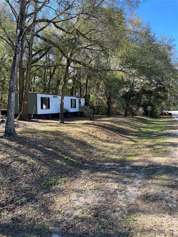 A single-story mobile home sits on a wooded lot next to a dirt road — 6359 VASSAR DRIVE, KEYSTONE HEIGHTS, FL