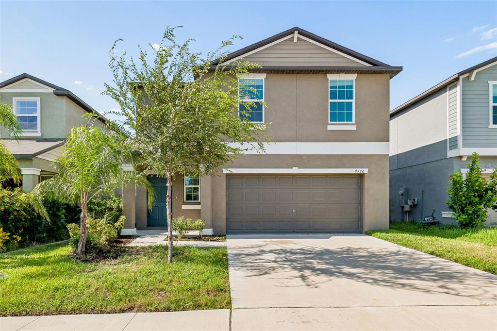 A two-story suburban house with a tan stucco exterior, a two-car garage, and a tree — 9920 SPANISH LIME COURT, RIVERVIEW, FL