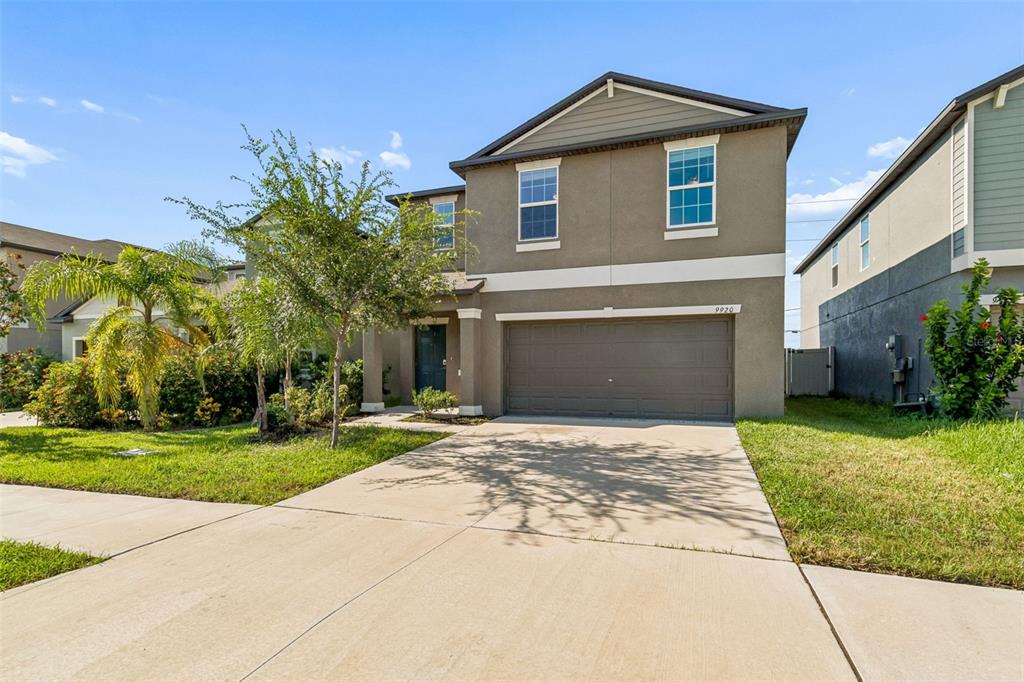 A two-story house with a beige stucco exterior, a two-car garage, and a concrete driveway — 9920 SPANISH LIME COURT, RIVERVIEW, FL