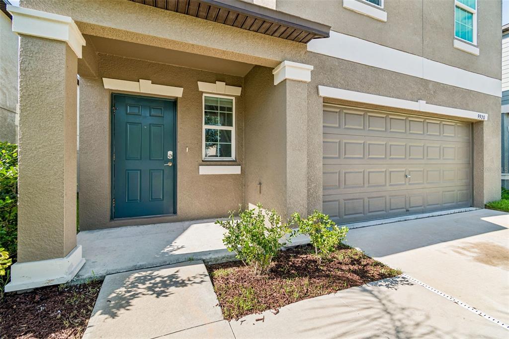 A tan two-story house exterior features a dark blue front door and a garage — 9920 SPANISH LIME COURT, RIVERVIEW, FL