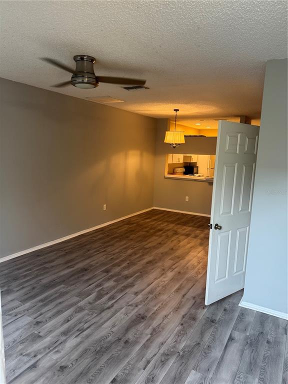 A living area with gray wood-look flooring, a ceiling fan, and an open kitchen pass-through — 30059 GRANDA HILLS COURT, WESLEY CHAPEL, FL