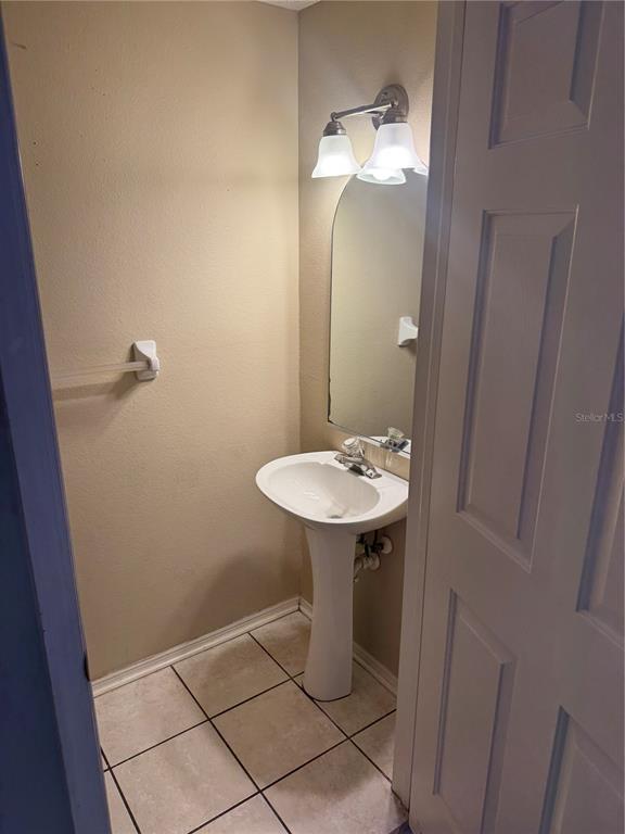 A small bathroom features a pedestal sink, an arched mirror, and a two-light vanity fixture — 30059 GRANDA HILLS COURT, WESLEY CHAPEL, FL