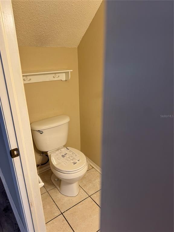 A small bathroom with a white toilet, tiled floor, and a wall-mounted shelf with hooks — 30059 GRANDA HILLS COURT, WESLEY CHAPEL, FL