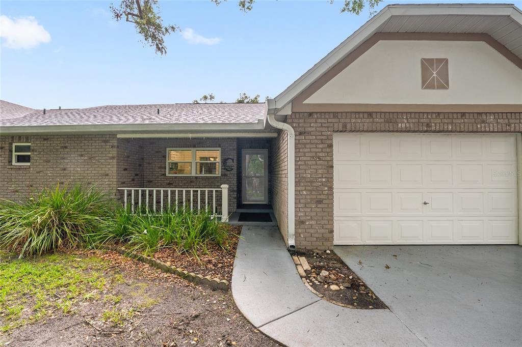 The exterior of a single-story brick house features a garage, a front porch, and landscaping — 9382 SW 89TH COURT ROAD UNIT C, OCALA, FL