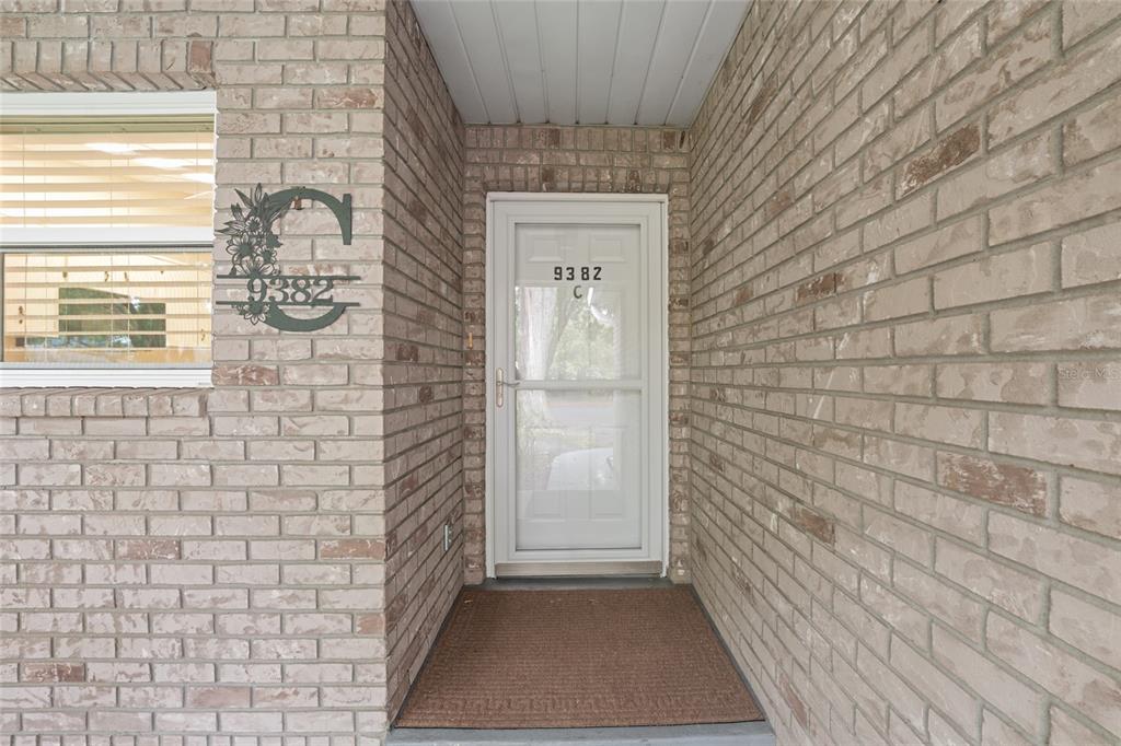 A brick exterior entryway features a white storm door and a decorative metal wall sign — 9382 SW 89TH COURT ROAD UNIT C, OCALA, FL