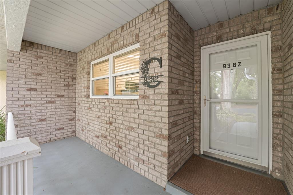 A brick-walled front porch features a white storm door and a decorative metal house number — 9382 SW 89TH COURT ROAD UNIT C, OCALA, FL
