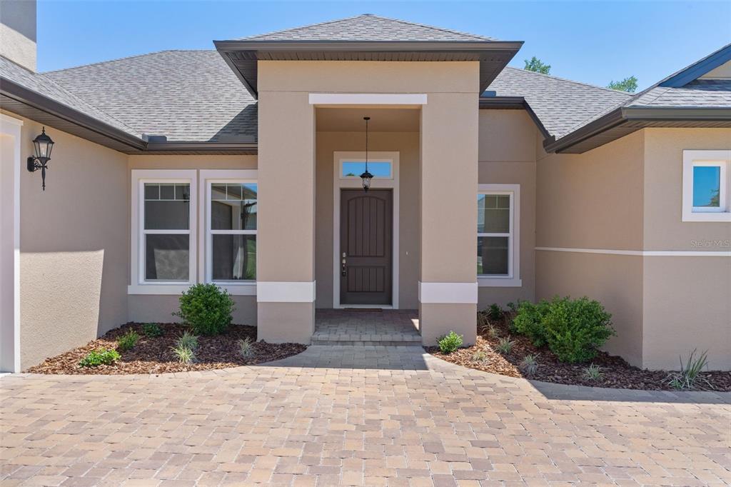 The exterior of a house features a tan stucco facade, a dark door, and a paver driveway — 39654 GROVE HEIGHTS, LADY LAKE, FL