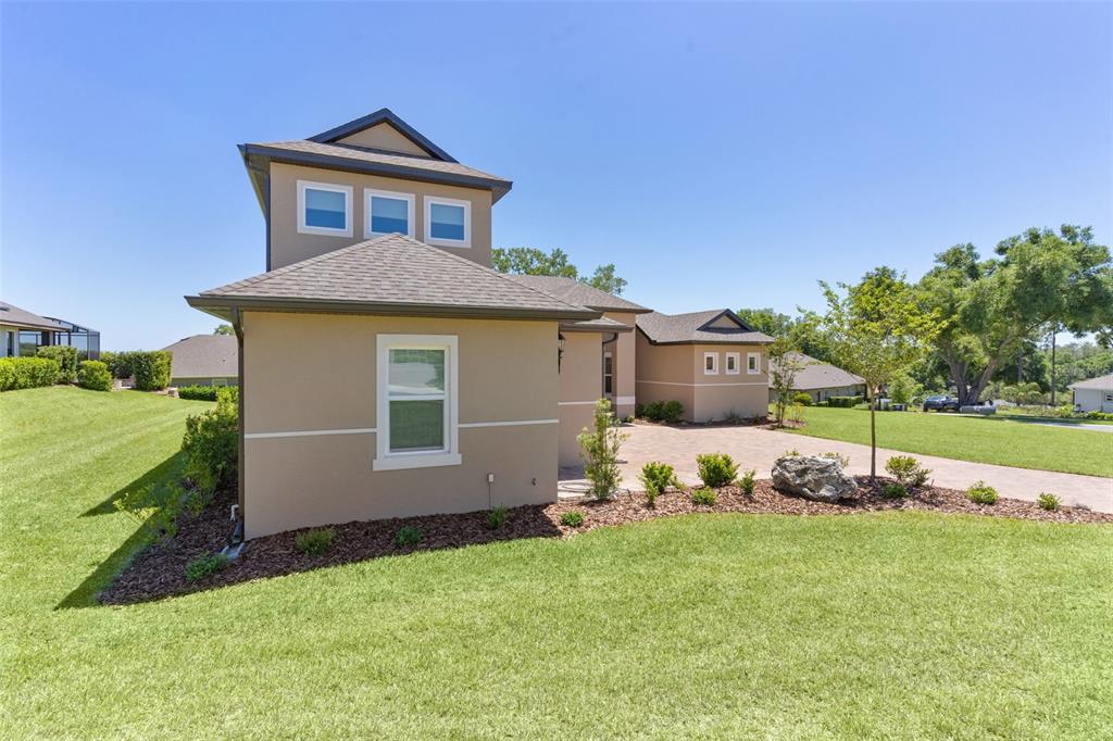 A tan stucco house with a multi-level roof and a paved driveway sits on grass — 39654 GROVE HEIGHTS, LADY LAKE, FL