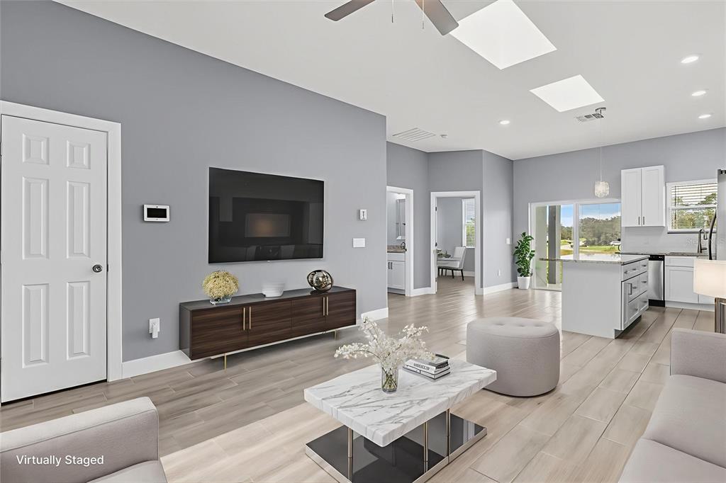 A living room with gray walls, wood-look tile floors, a television, and an open kitchen — 423 VERNON COURT, KISSIMMEE, FL