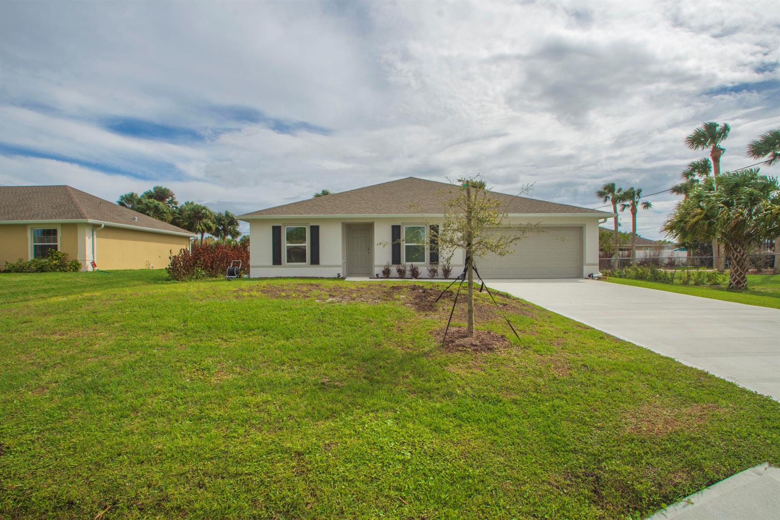 A single-story house with a beige exterior, dark shutters, a two-car garage, and a lawn — 450 Kendall Avenue, Sebastian FL 32958, SEBASTIAN, FL