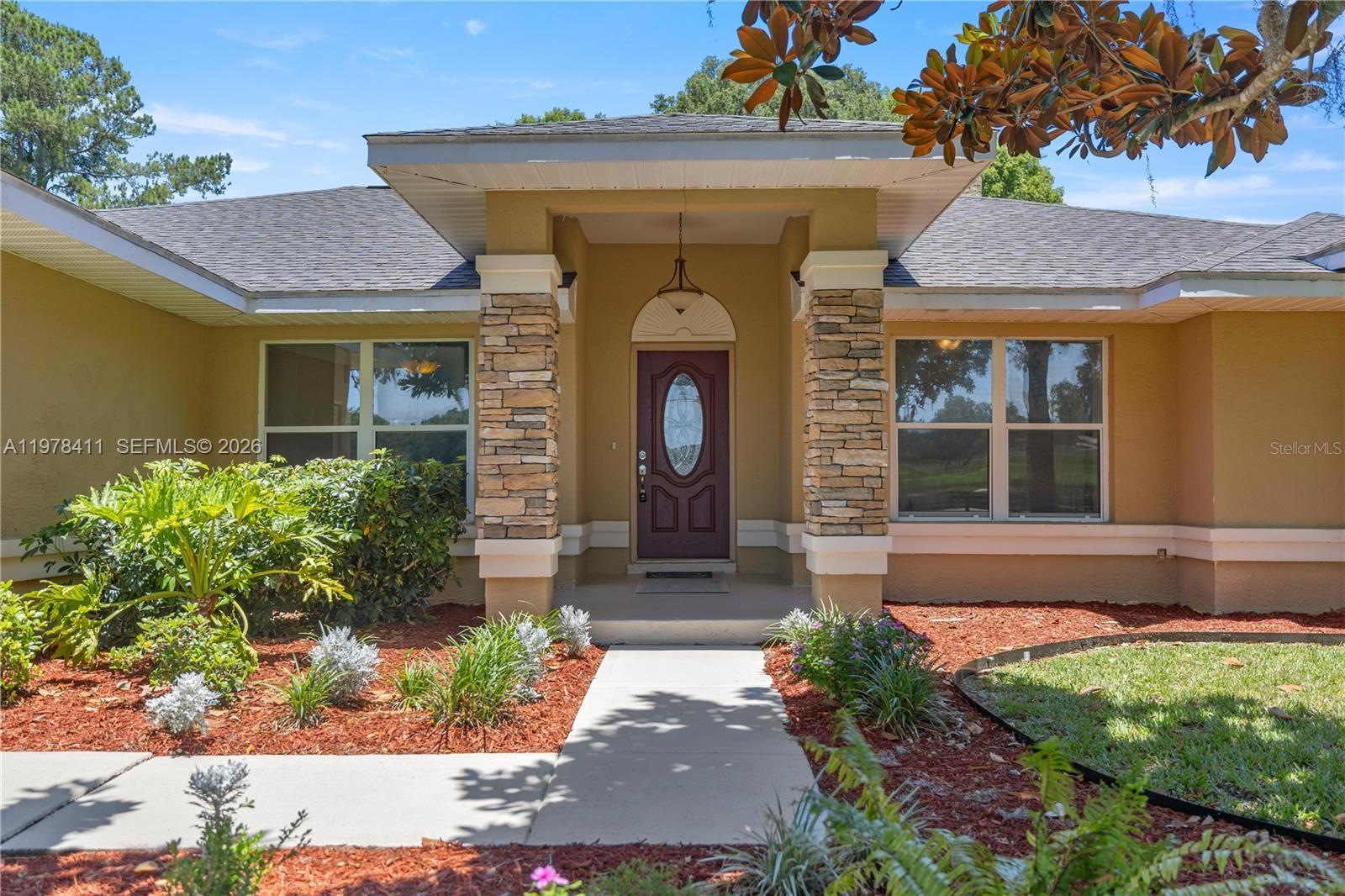 The exterior of a single-story house features a stone-columned entryway and a dark red door — 1699 SW 80, Ocala FL 34476, OCALA, FL