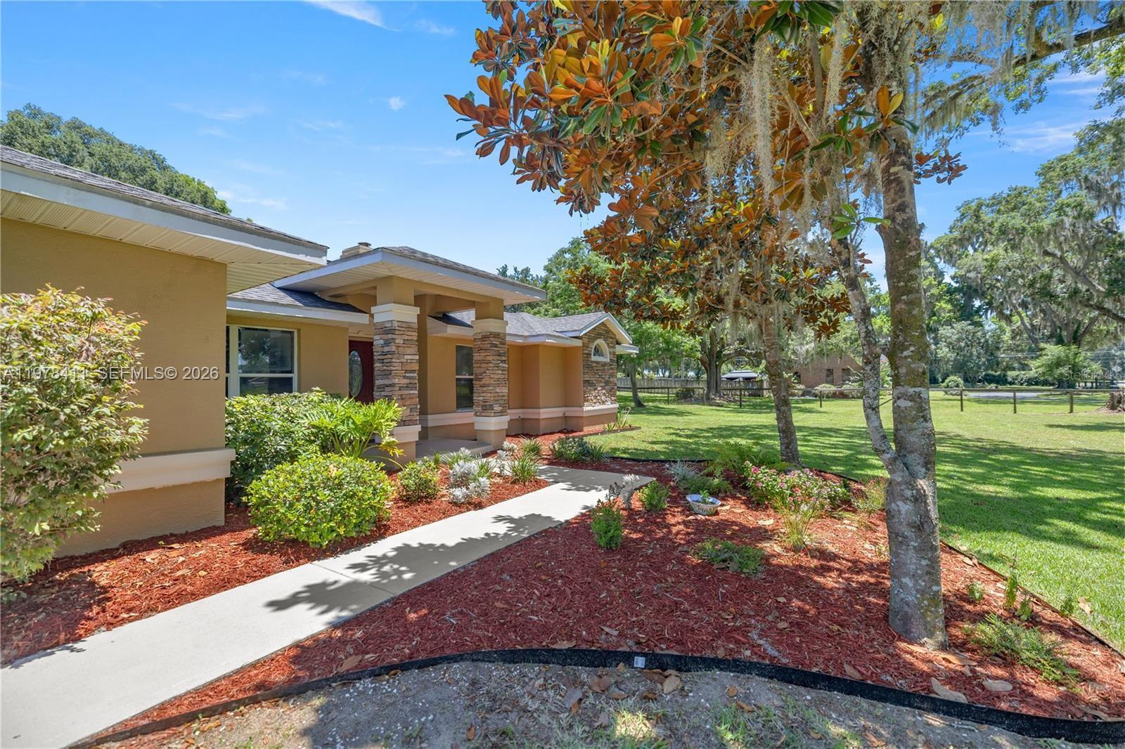 A tan house with stone columns and a concrete walkway sits on a grassy lot — 1699 SW 80, Ocala FL 34476, OCALA, FL