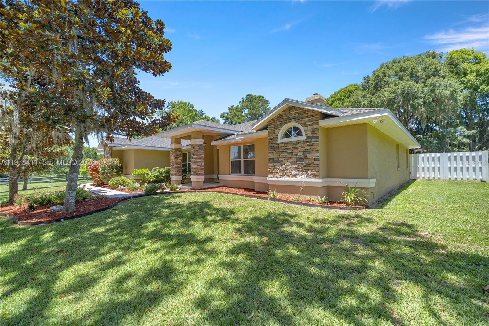 A single-story house with a stone-accented facade, tan stucco walls, and a grassy front yard — 1699 SW 80, Ocala FL 34476, OCALA, FL