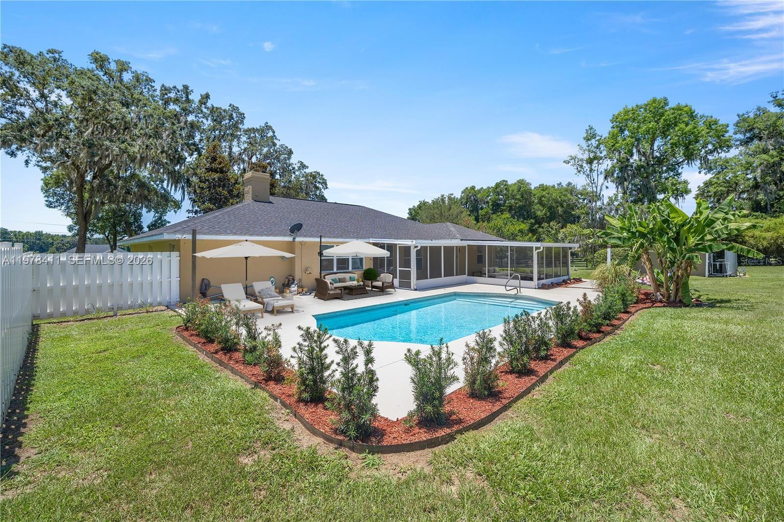 A backyard features a swimming pool, a patio with outdoor furniture, and a white fence — 1699 SW 80, Ocala FL 34476, OCALA, FL