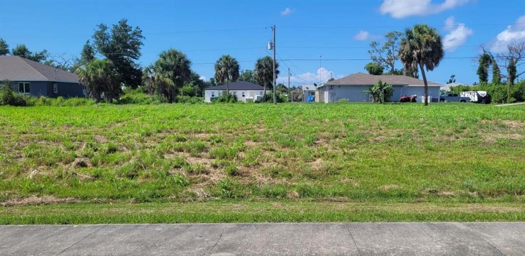 A vacant, grassy residential lot sits in front of several houses under a blue sky — 4435 S ACCESS ROAD, ENGLEWOOD, FL