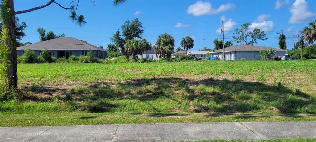 A vacant, grassy residential lot sits between two single-story houses under a blue sky — 4435 S ACCESS ROAD, ENGLEWOOD, FL