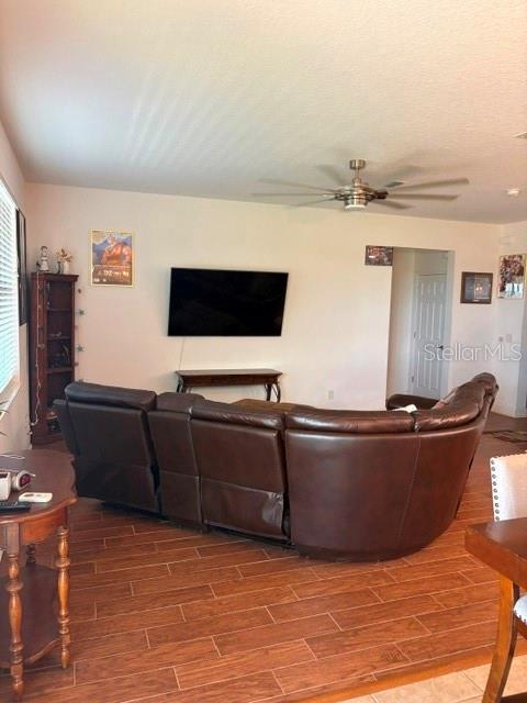 A living room features a large brown sectional sofa, a wall-mounted television, and wood-look flooring — 9819 ROYAL VISTA AVENUE, CLERMONT, FL