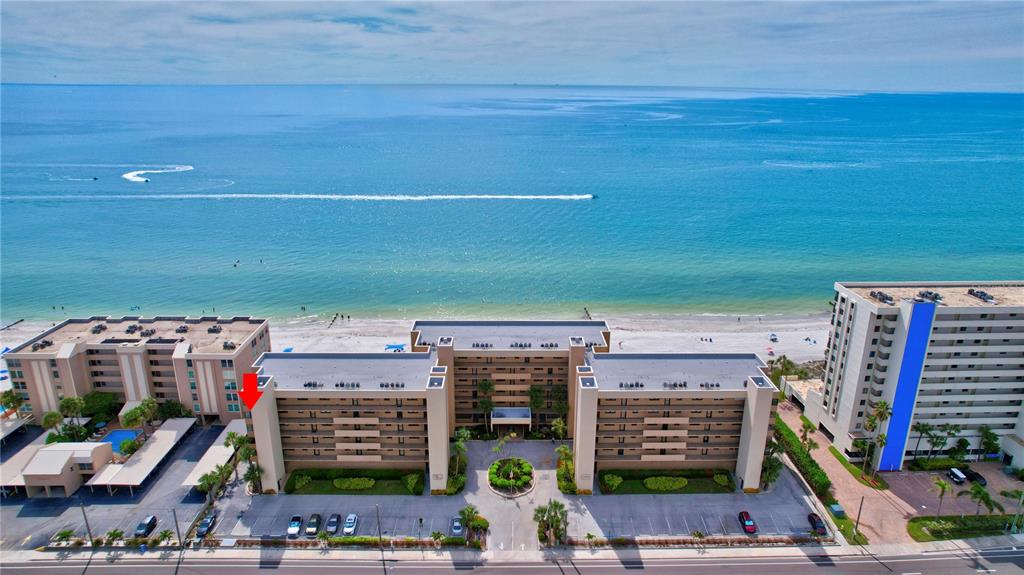An aerial view shows a multi-story beachfront condominium complex with a parking lot and ocean — 14900 GULF BOULEVARD UNIT 401, MADEIRA BEACH, FL