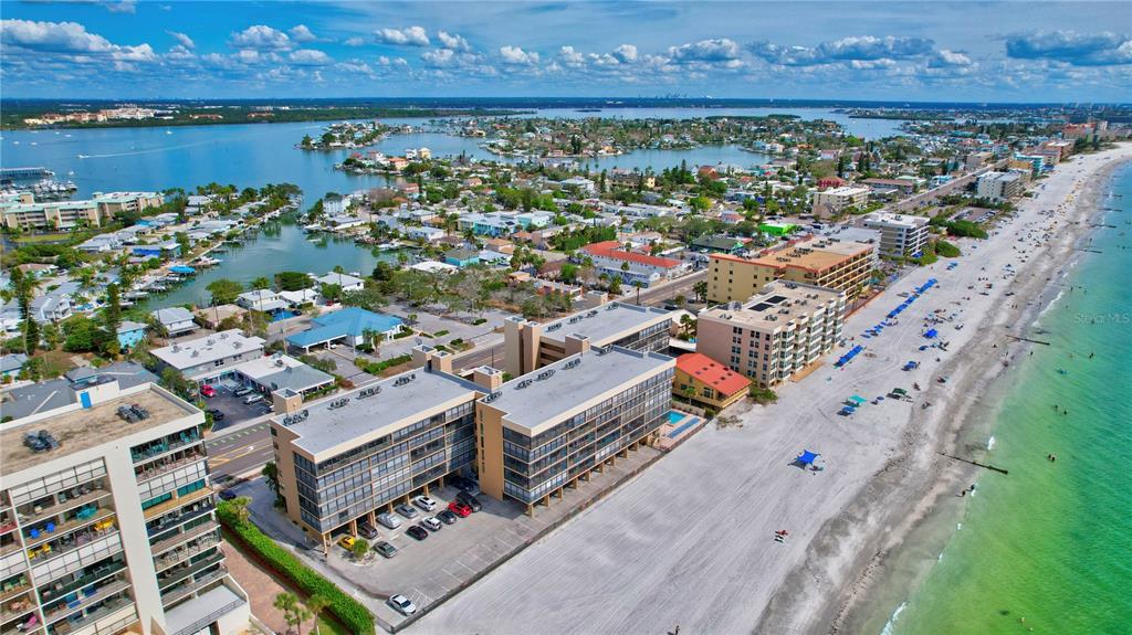 An aerial view shows beachfront apartment buildings, a sandy beach, and a coastal bay — 14900 GULF BOULEVARD UNIT 401, MADEIRA BEACH, FL