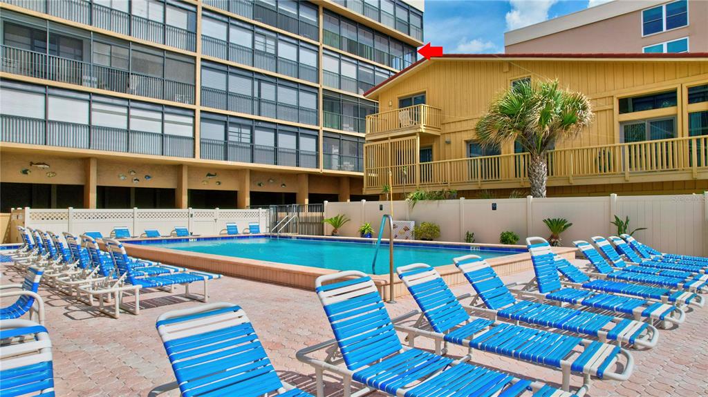 A swimming pool surrounded by lounge chairs sits in front of a multi-story apartment building — 14900 GULF BOULEVARD UNIT 401, MADEIRA BEACH, FL