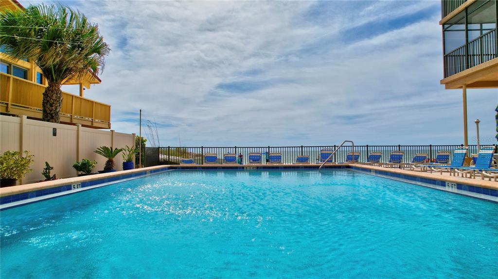 A rectangular swimming pool sits on a patio overlooking the ocean with lounge chairs nearby — 14900 GULF BOULEVARD UNIT 401, MADEIRA BEACH, FL