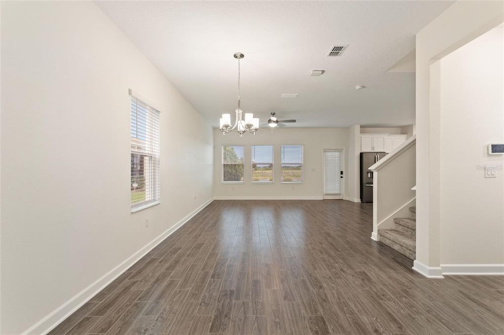 An open-concept living area features wood-look tile flooring, a chandelier, and a carpeted staircase — 8801 BETH PAGE LANE, DAVENPORT, FL