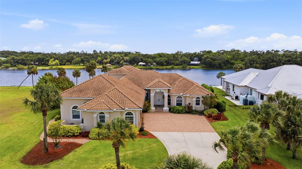 An aerial view shows a tan house with a tiled roof situated beside a lake — 2504 CALOOSA SHORES DRIVE, LABELLE, FL