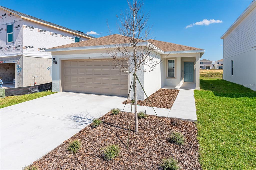 A single-story house with a tan garage, light blue front door, and adjacent construction site — 3633 CAMBRIDGE BROOK DRIVE, DAVENPORT, FL