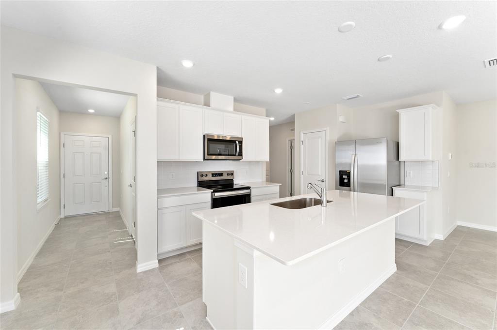 A modern kitchen features white cabinetry, stainless steel appliances, a center island, and tile flooring — 3633 CAMBRIDGE BROOK DRIVE, DAVENPORT, FL