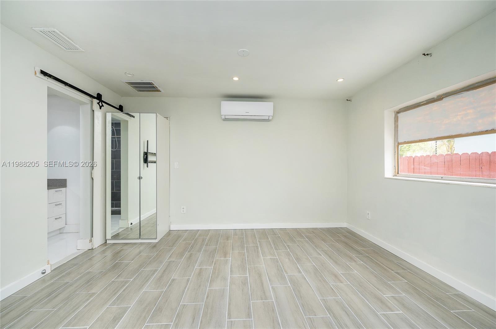 A room with light-colored walls, wood-look tile flooring, a mini-split unit, and a mirrored door — 10954 SW 157th Ter # 1, Miami FL 33157, MIAMI, FL