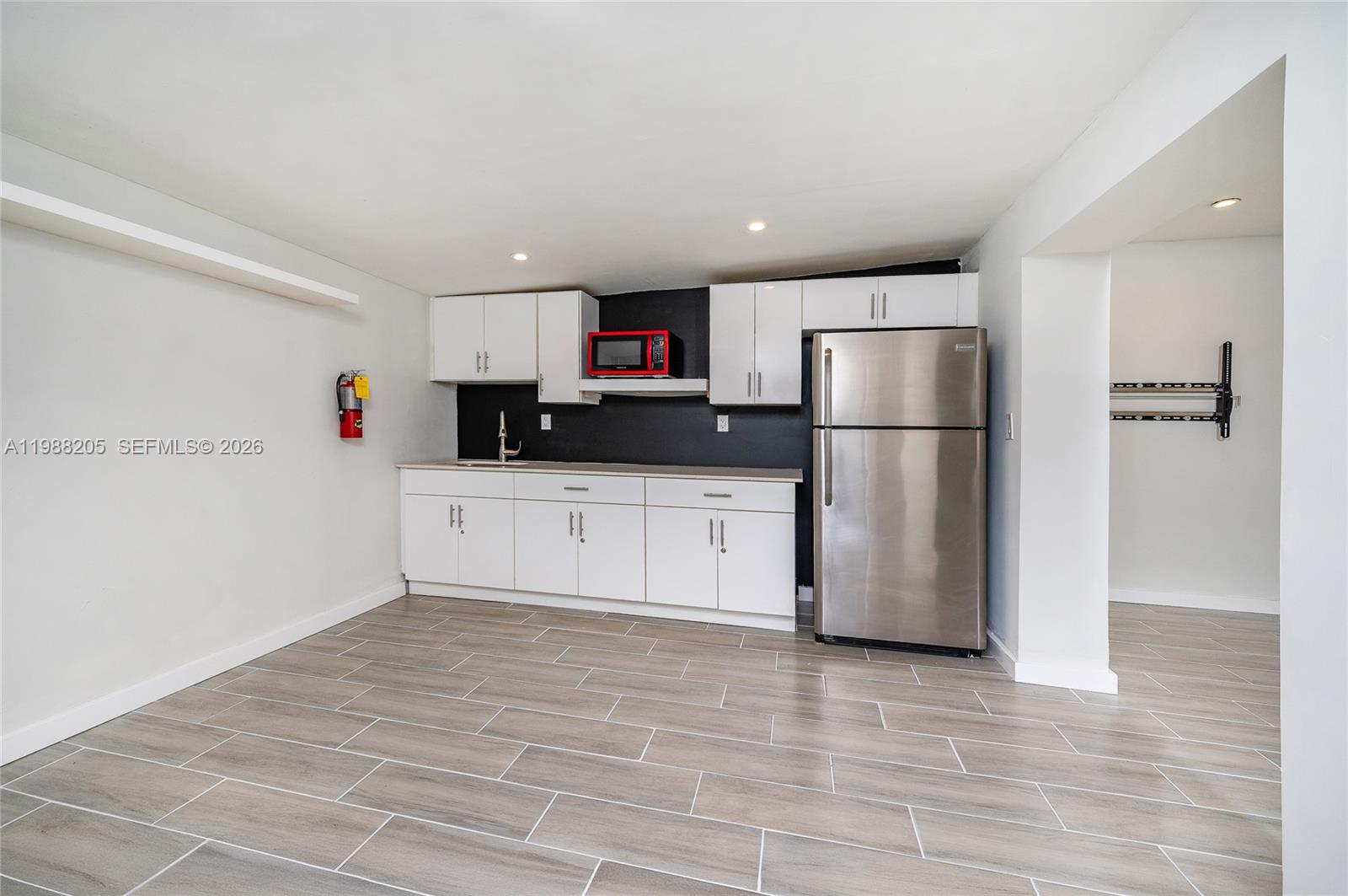 A kitchen area features white cabinets, stainless steel appliances, and gray wood-look tile flooring — 10954 SW 157th Ter # 1, Miami FL 33157, MIAMI, FL