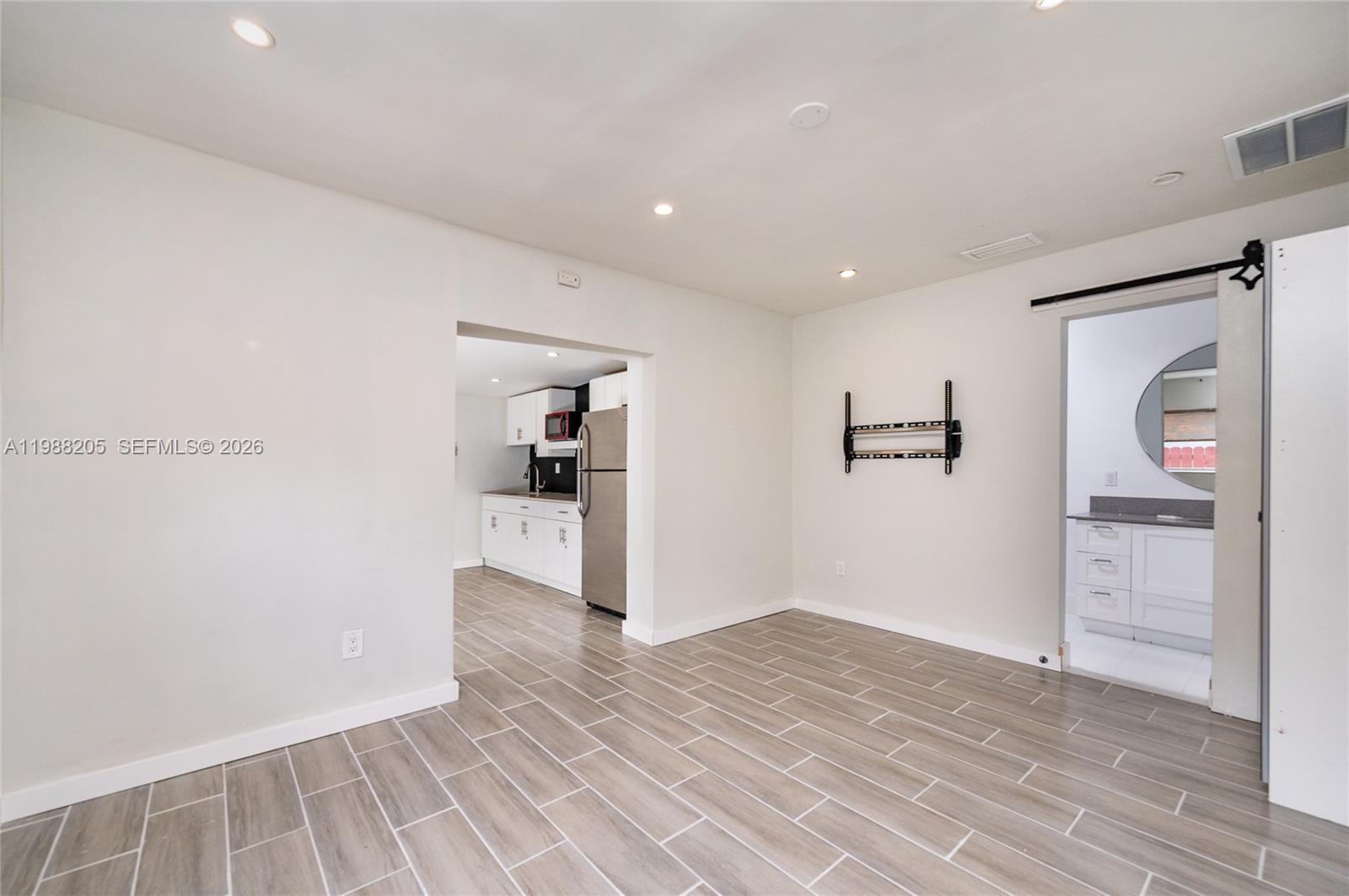 A room with light-colored walls, wood-look tile flooring, a kitchen doorway, and a sliding door — 10954 SW 157th Ter # 1, Miami FL 33157, MIAMI, FL