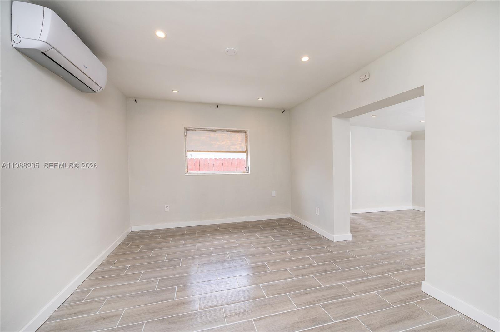 An empty room features light-colored tile flooring, white walls, and a wall-mounted air conditioning unit — 10954 SW 157th Ter # 1, Miami FL 33157, MIAMI, FL