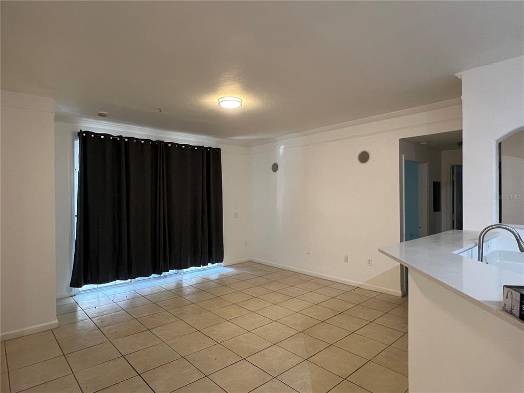 An empty room with beige tile flooring, white walls, and dark curtains over a sliding door — 6685 QUEENS BOROUGH AVENUE UNIT 101, ORLANDO, FL