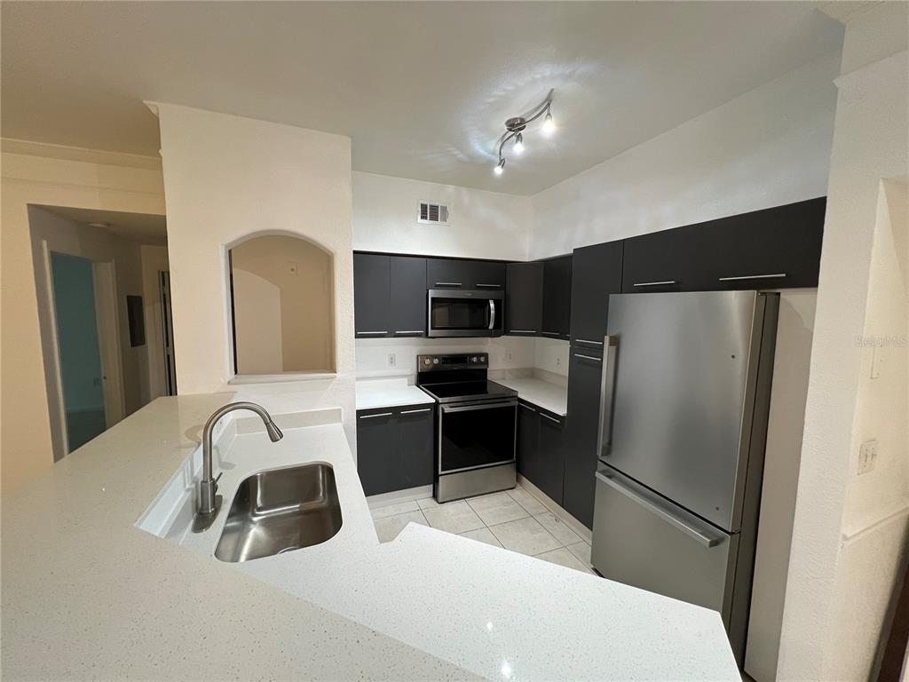 A kitchen features dark cabinets, stainless steel appliances, and white countertops with a breakfast bar — 6685 QUEENS BOROUGH AVENUE UNIT 101, ORLANDO, FL